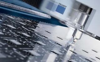 Laser cutting machine head cutting sheet metal on a CNC laser cutting bed, showing precision metal laser cutting with clean cut edges in a manufacturing workshop.