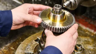 Close-up of machinist installing a steel gear with brass hub onto a spindle in a workshop setting.